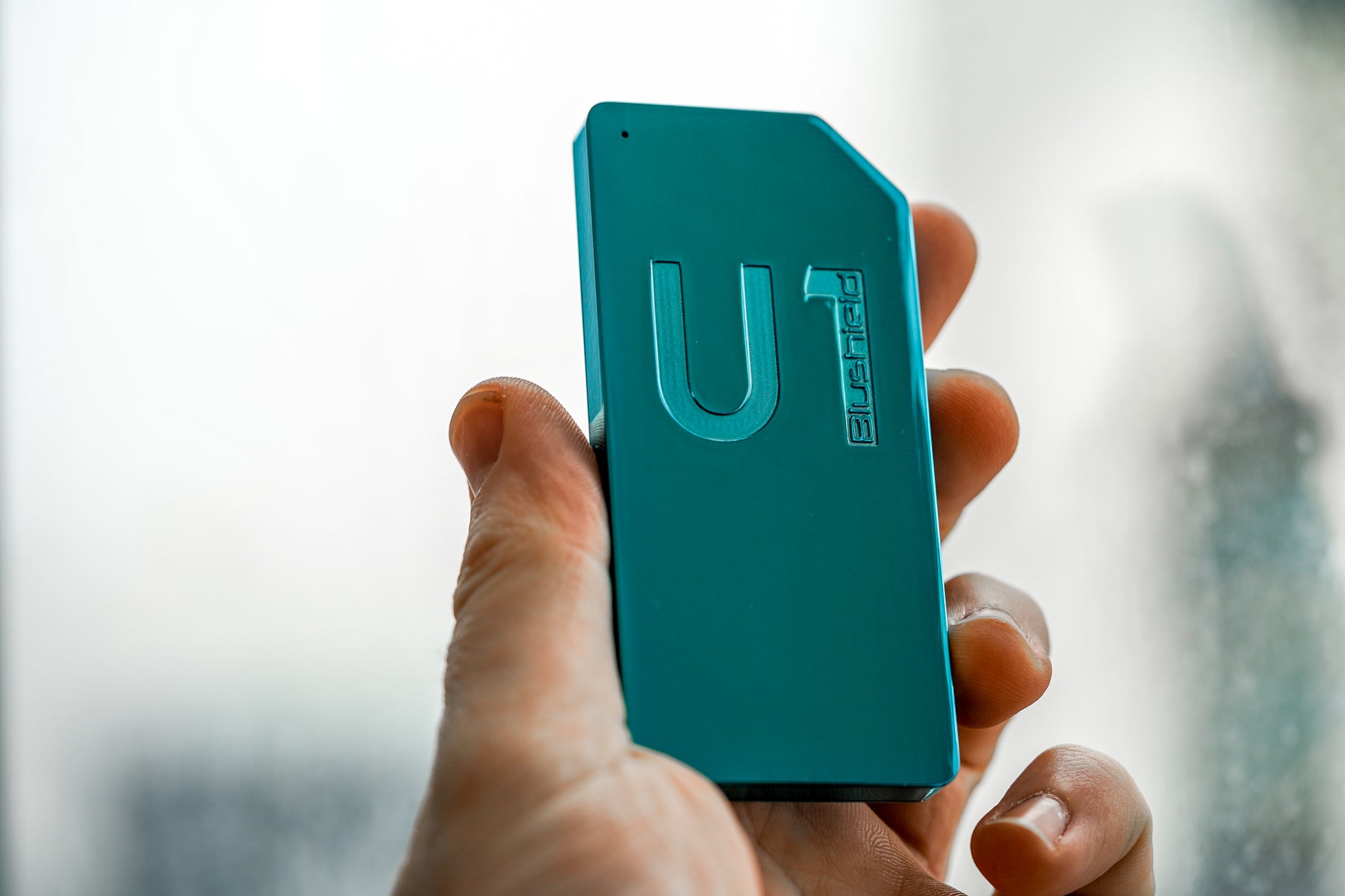 Teal U1 device held in a hand with a blurred background