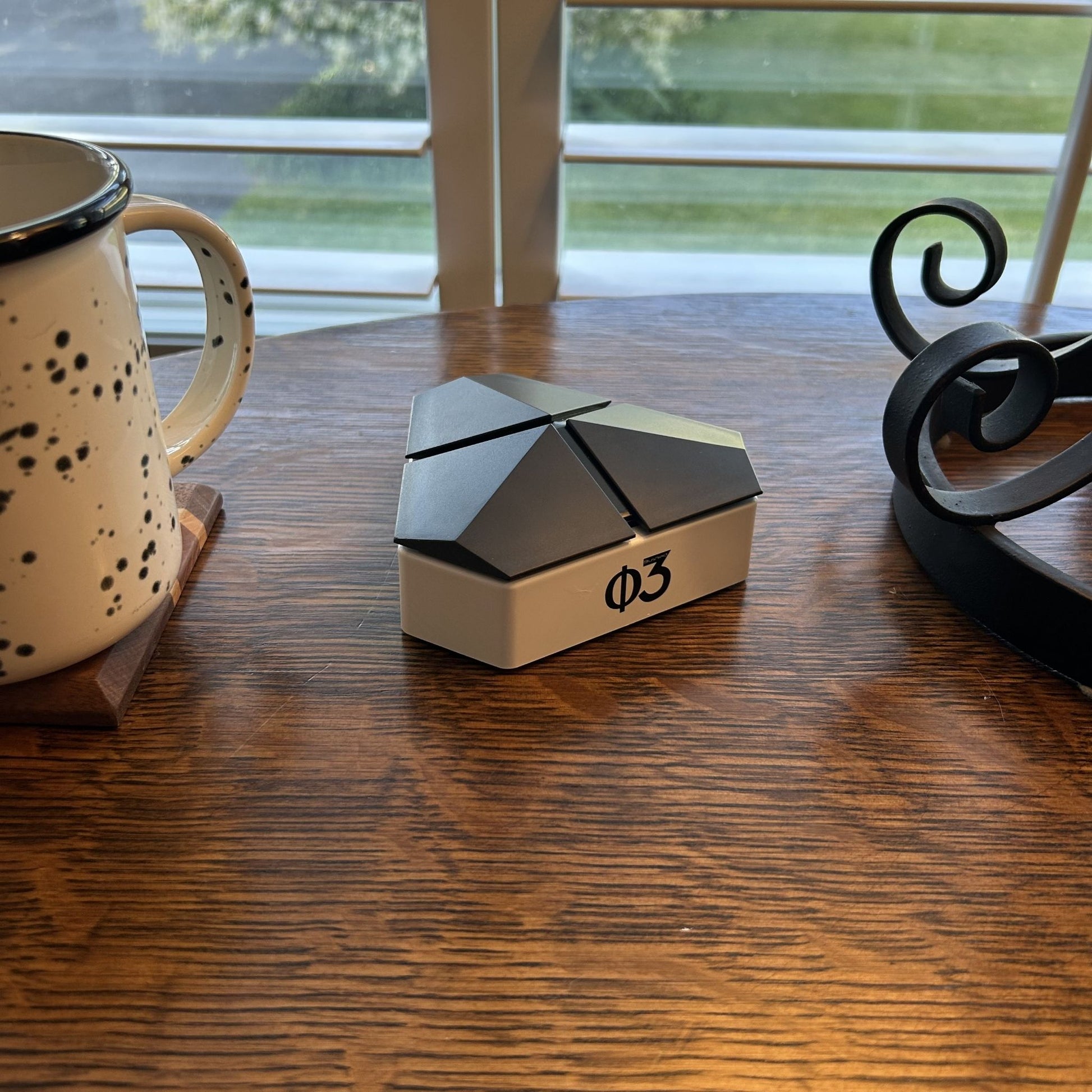 Blushield Phi 03 device on a wooden surface next to a speckled mug