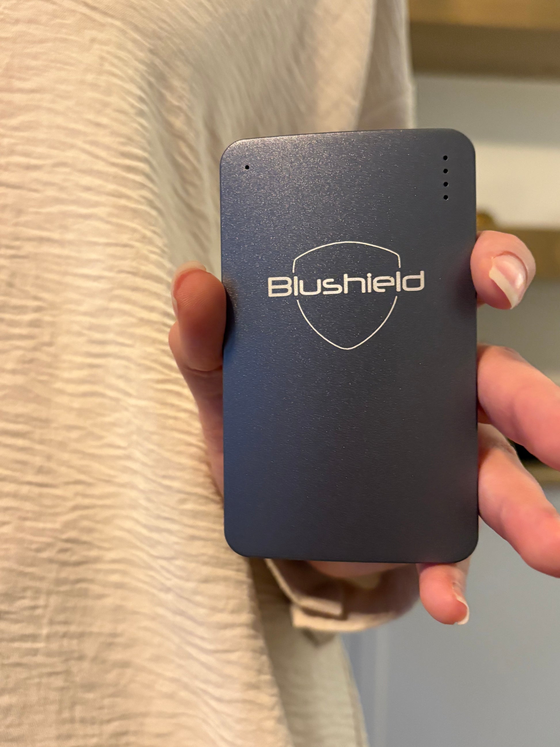 Hand holding a black Blushield Ultimate Portable on a beige surface.