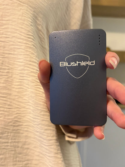 Hand holding a black Blushield Ultimate Portable on a beige surface.